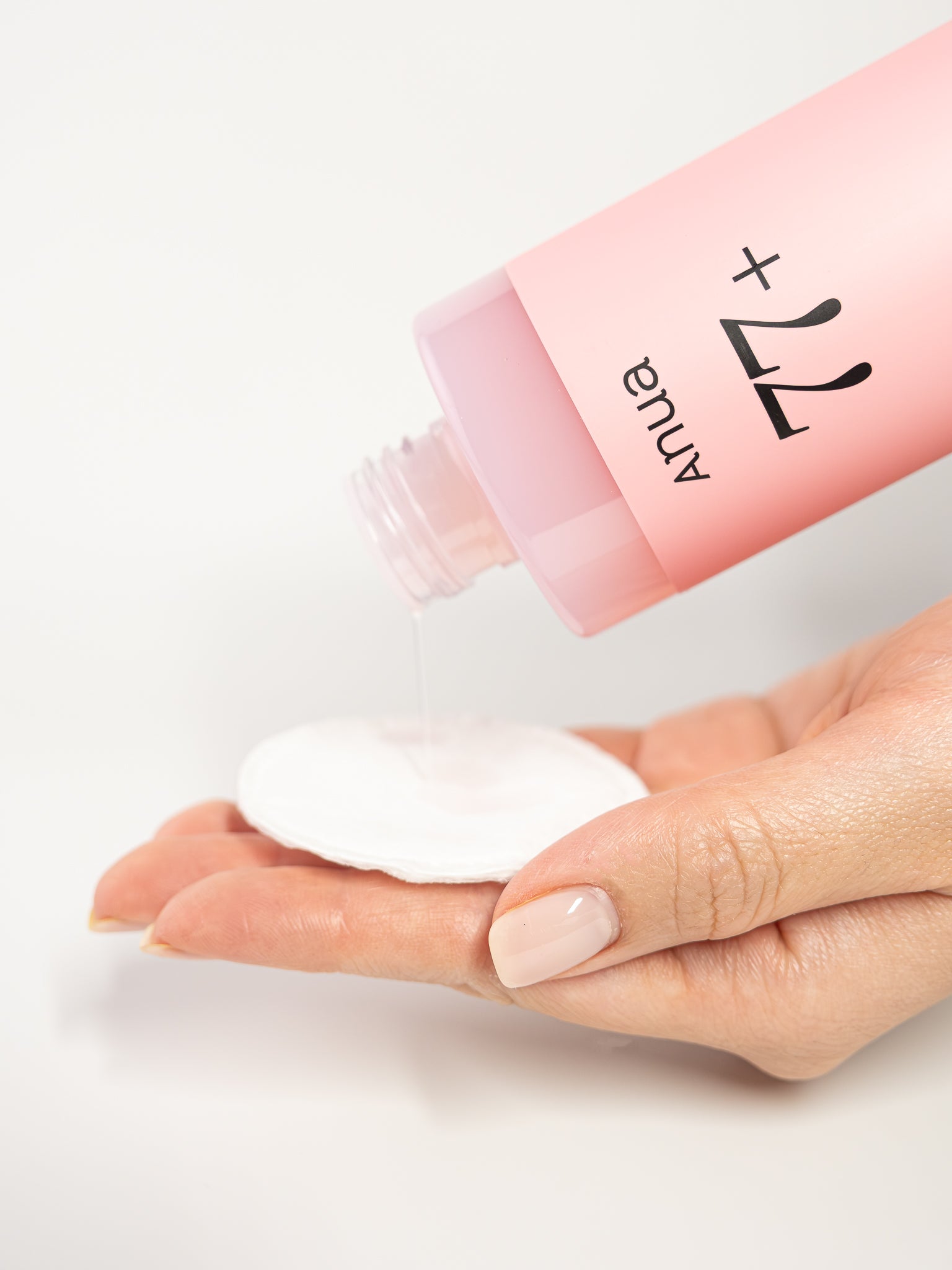 Hand holding a Pink bottle of anua 77+ essence toner pouring on to cotton pad