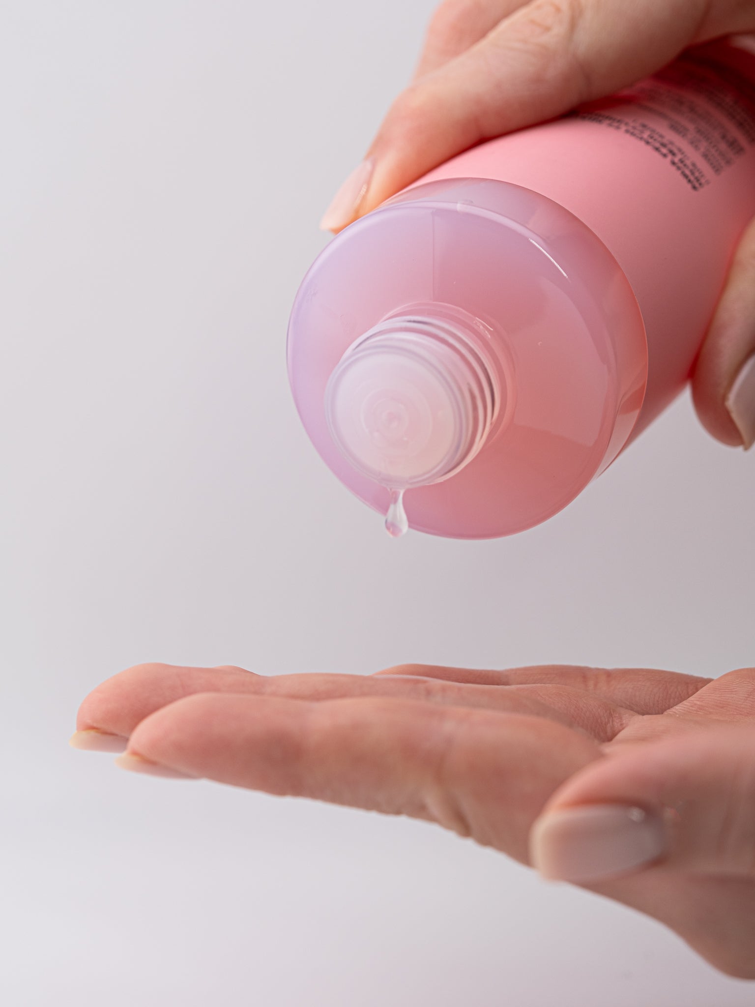 Hand holding peach 77+ niacin toner, dispensing toner onto another hand against a light gray background.