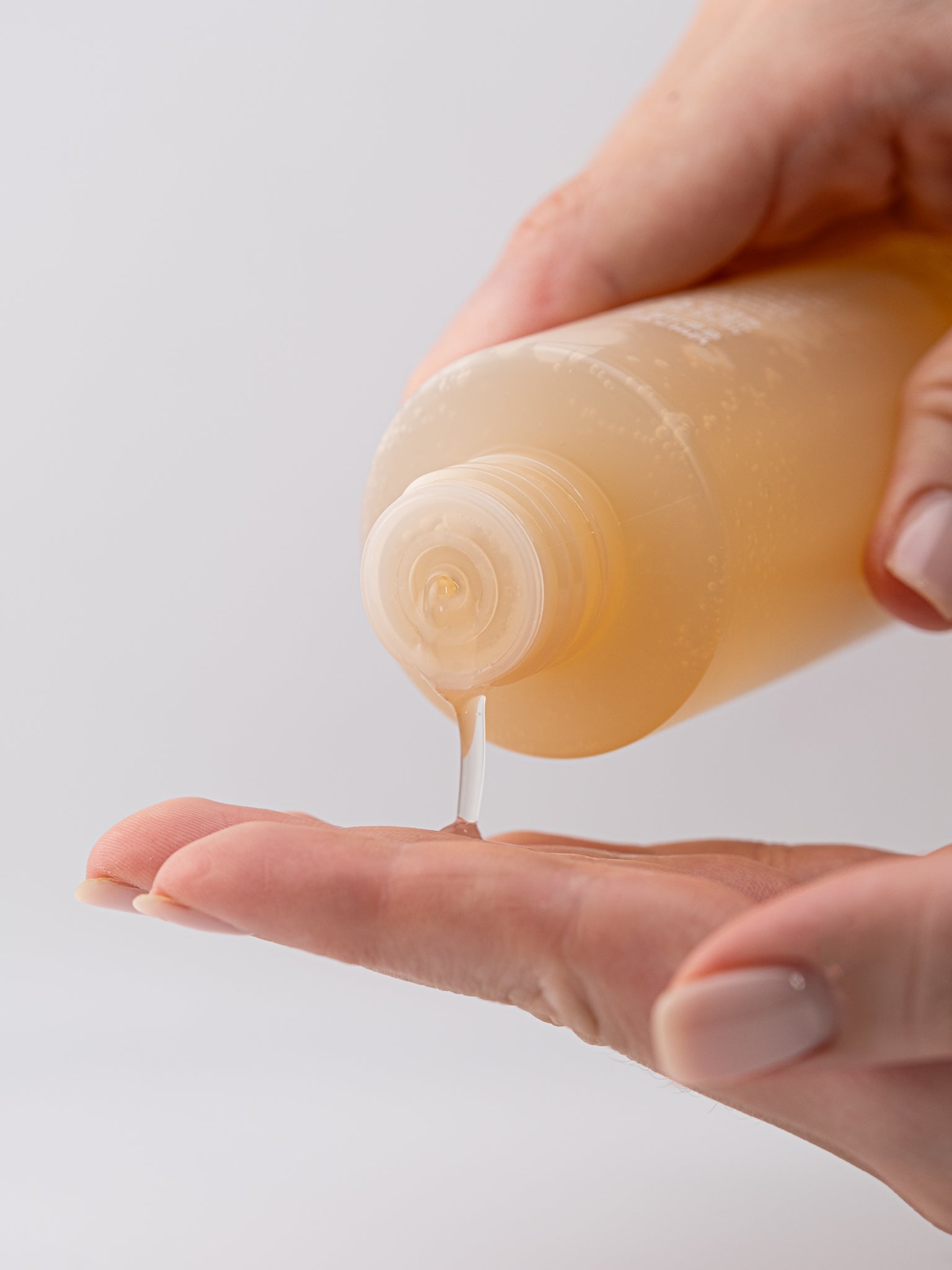 Hand holding a bottle of super glowing essence toner with a small amount dripping onto the palm against a light background