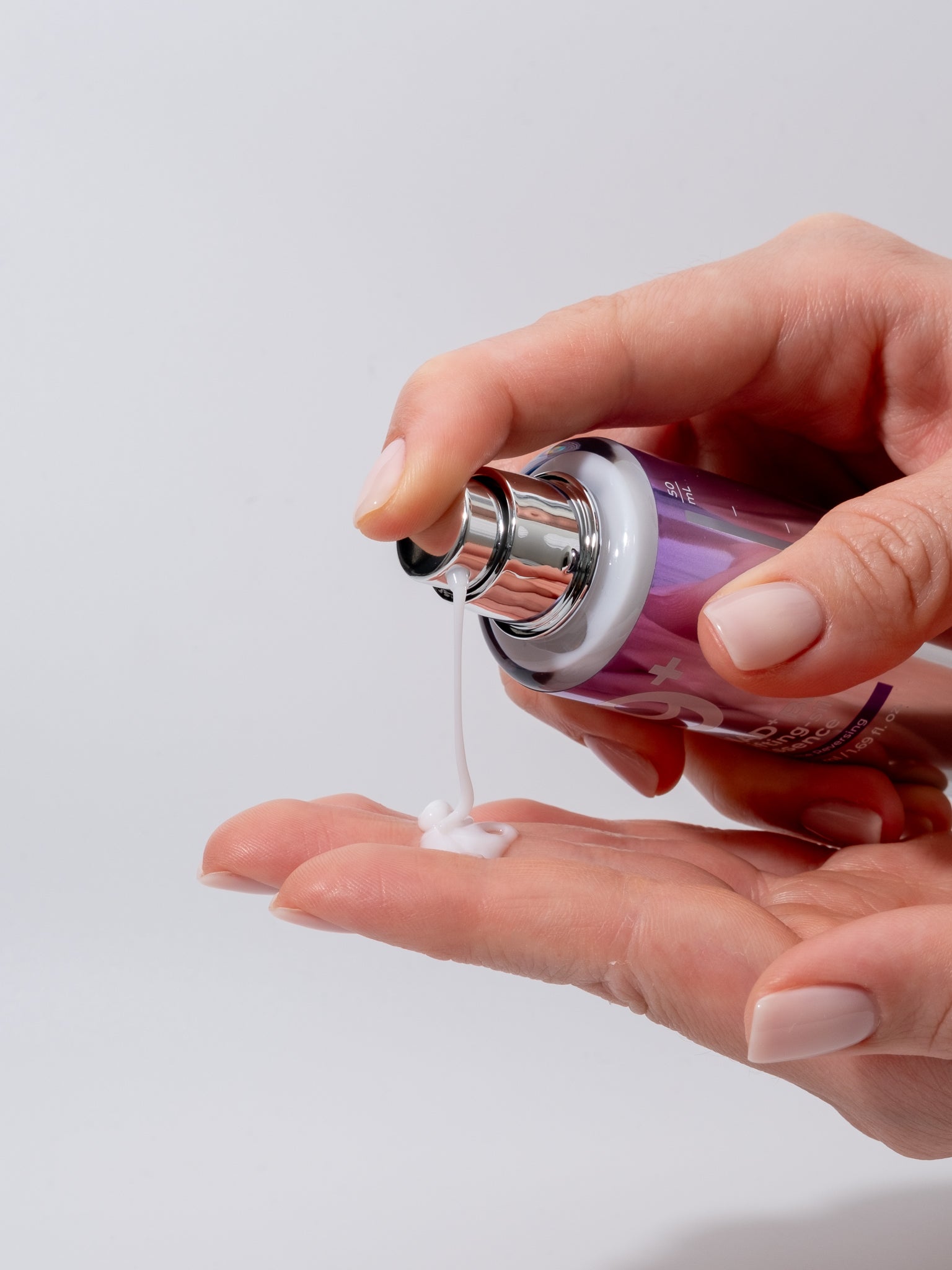 Hand holding numbuzin no9 nad bio lifting-sil essence with a white liquid being poured onto another hand against a light gray background