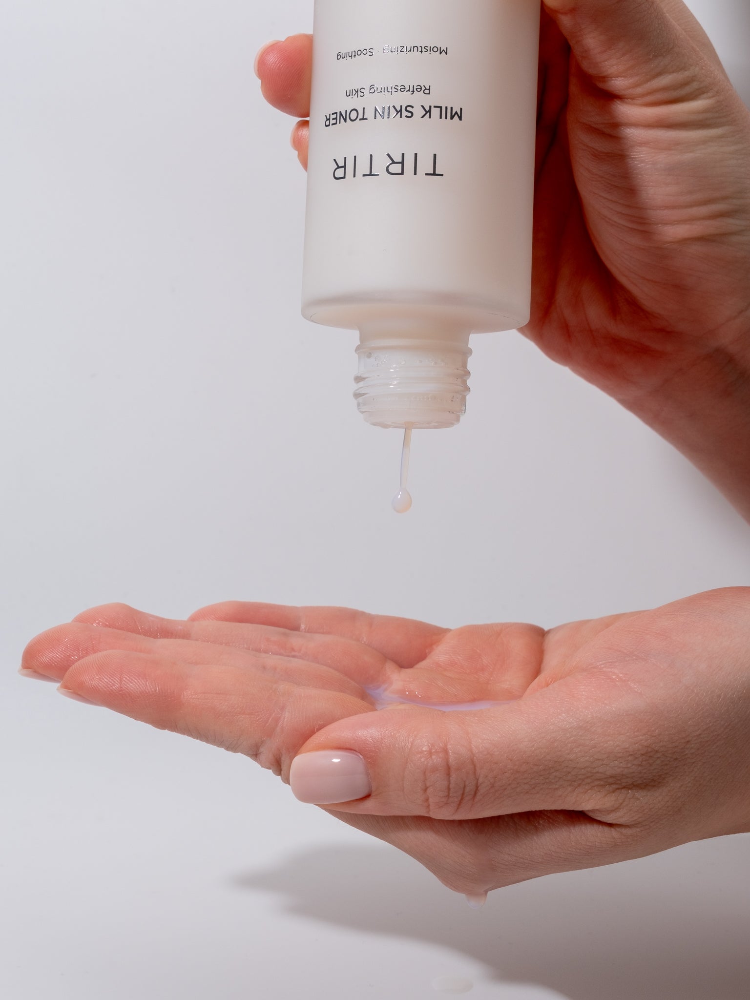 Hand holding a bottle of Tir Tir Milk Skin Toner with liquid dripping onto another hand against a white background