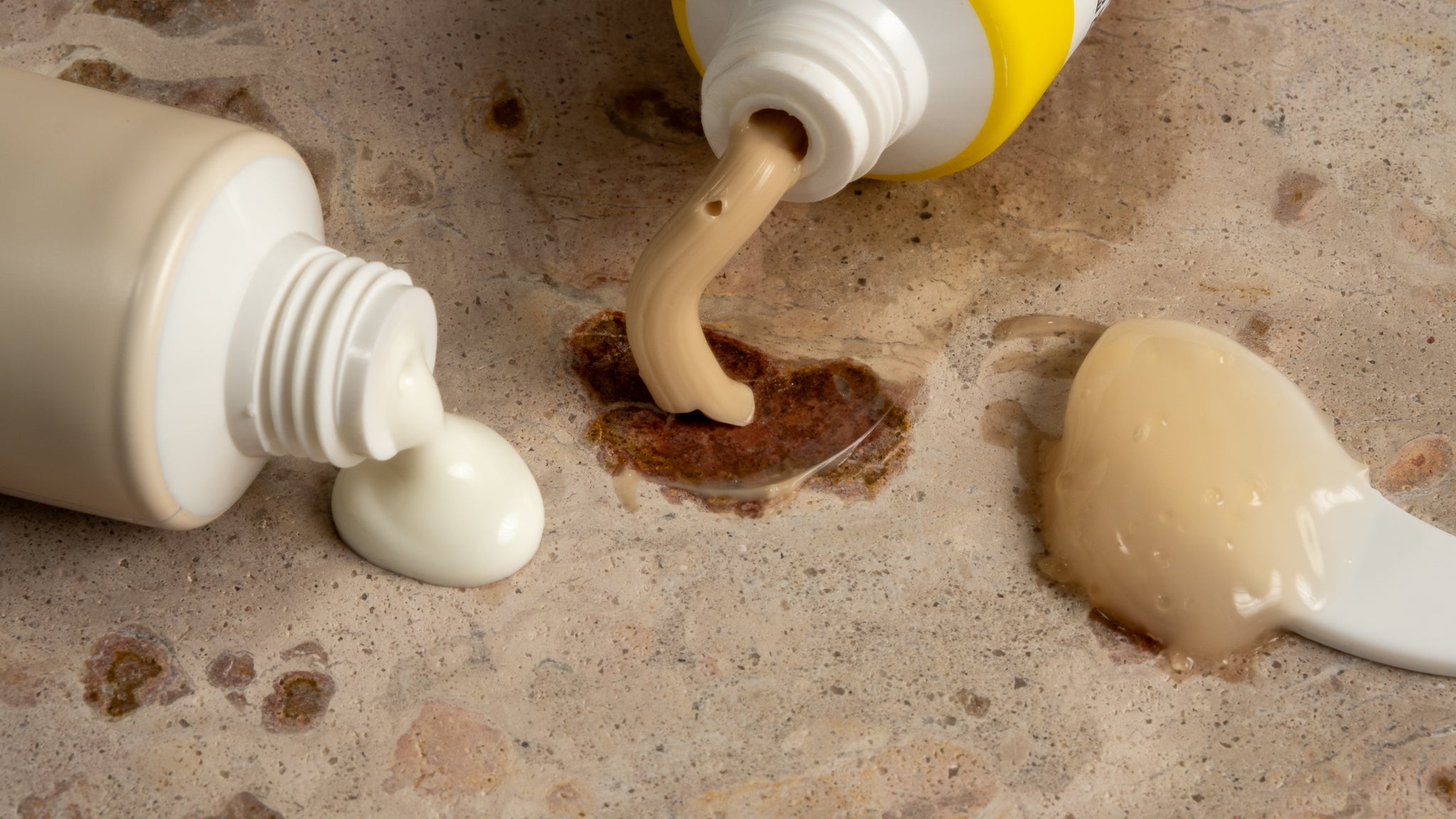 Two tubes of cream being squeezed onto a textured surface with visible residue.