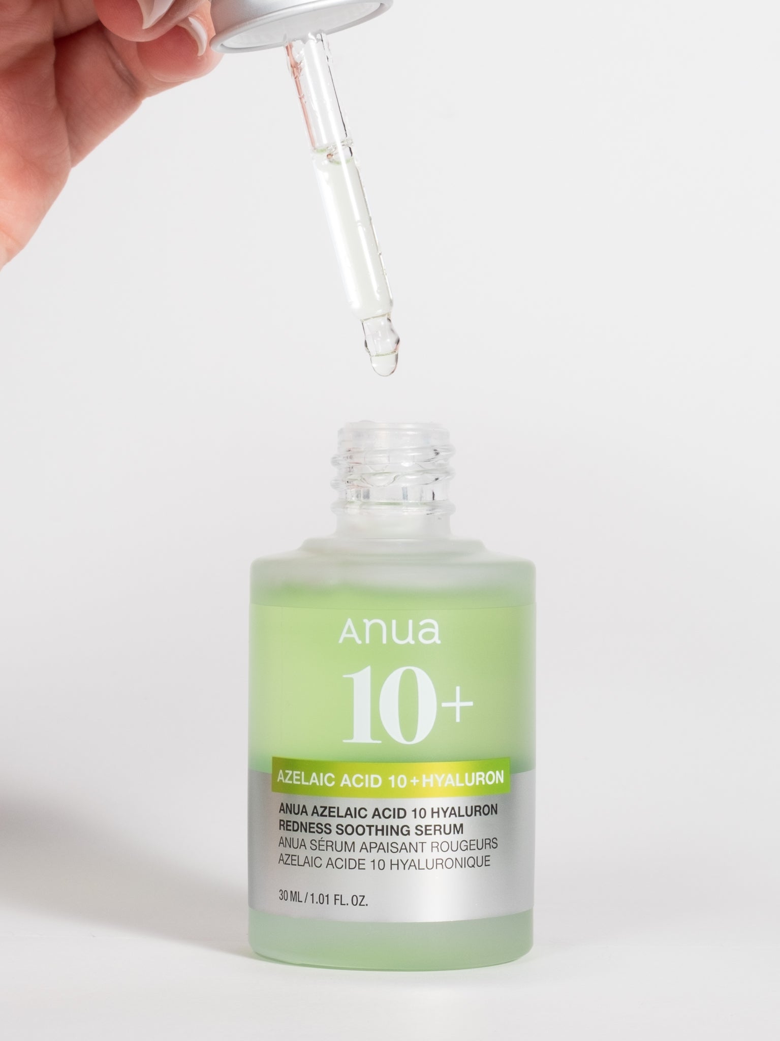 A hand holding a silver dropper with Anua Azelaic Acid 10 + Hyaluron Redness Soothing Serum over an open bottle of the same product.