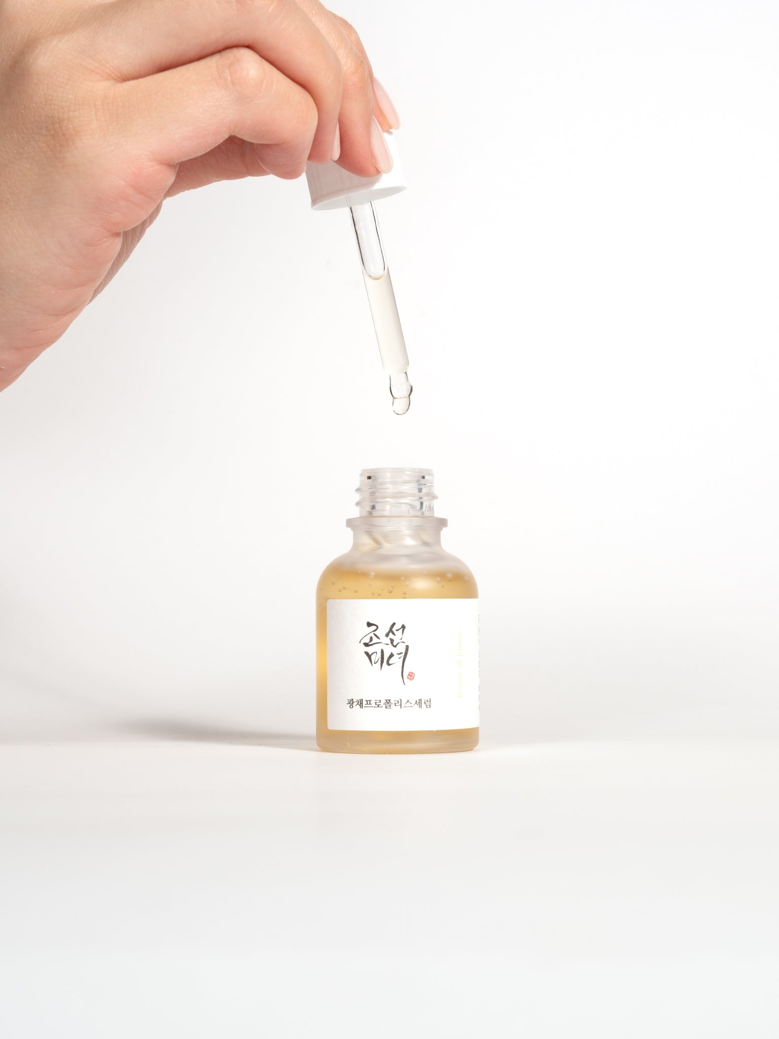 A hand holding a glass dropper filled with serum over an open bottle of Beauty of Joseon Glow Serum.