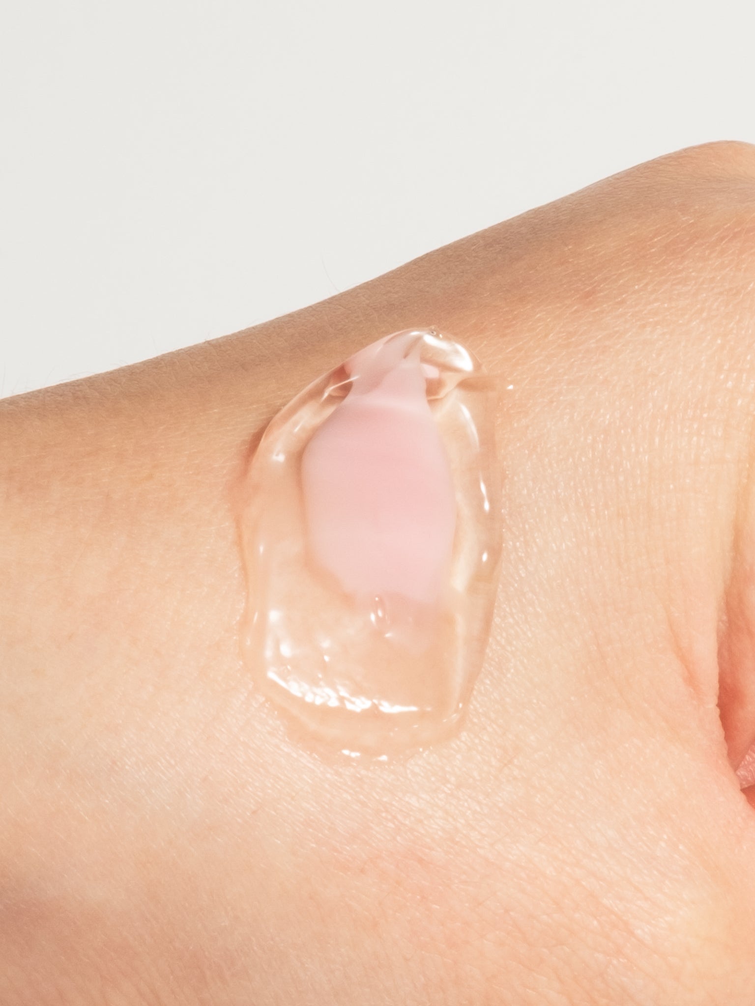 A close-up of a pink cream capsule and clear gel from the Medicube PDRN Pink Collagen Capsule Cream on the back of a hand.