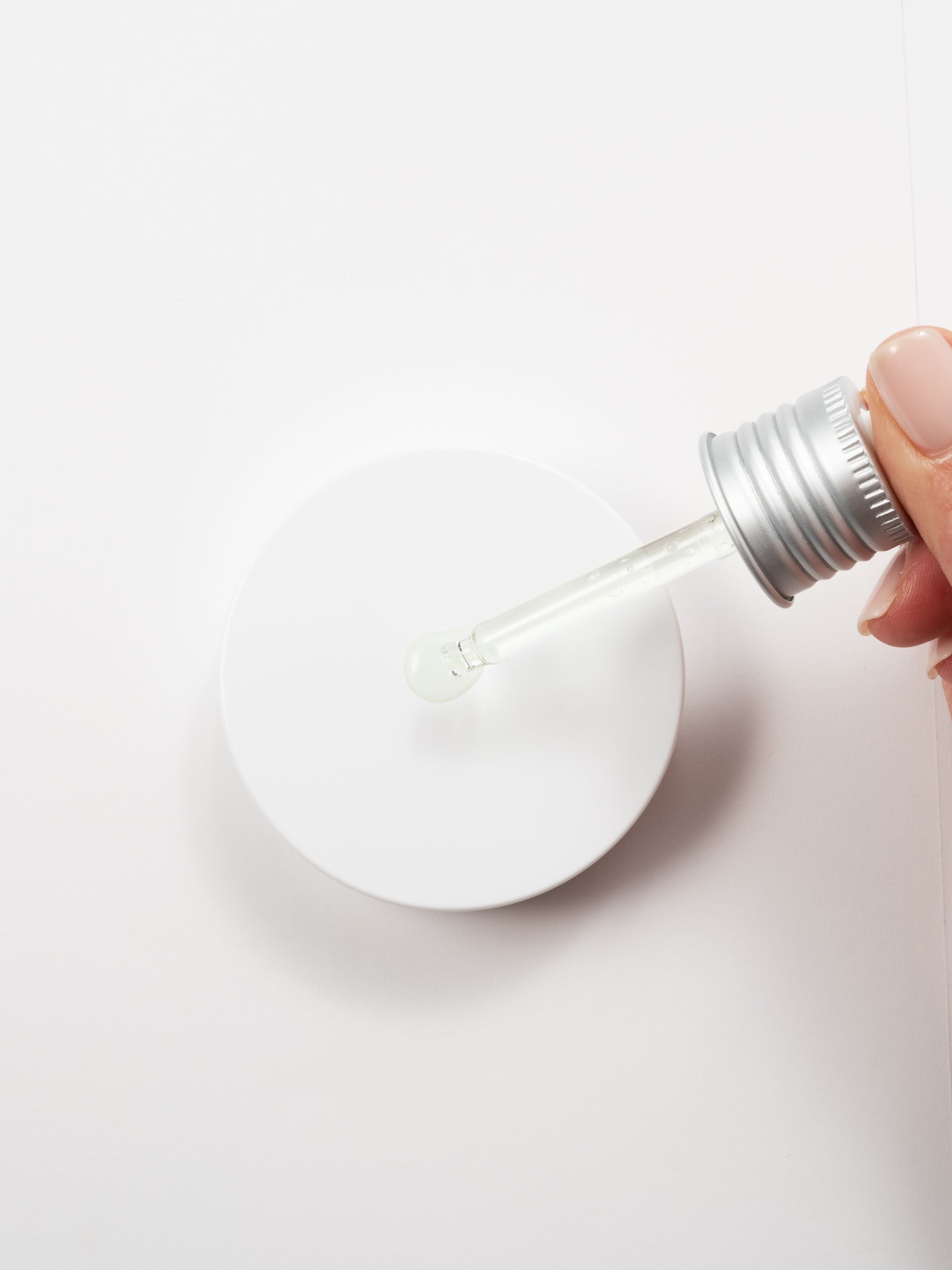 Macro view of a hand applying a drop of Anua Azelaic Acid 10 + Hyaluron Redness Soothing Serum from a silver dropper onto a white surface.
