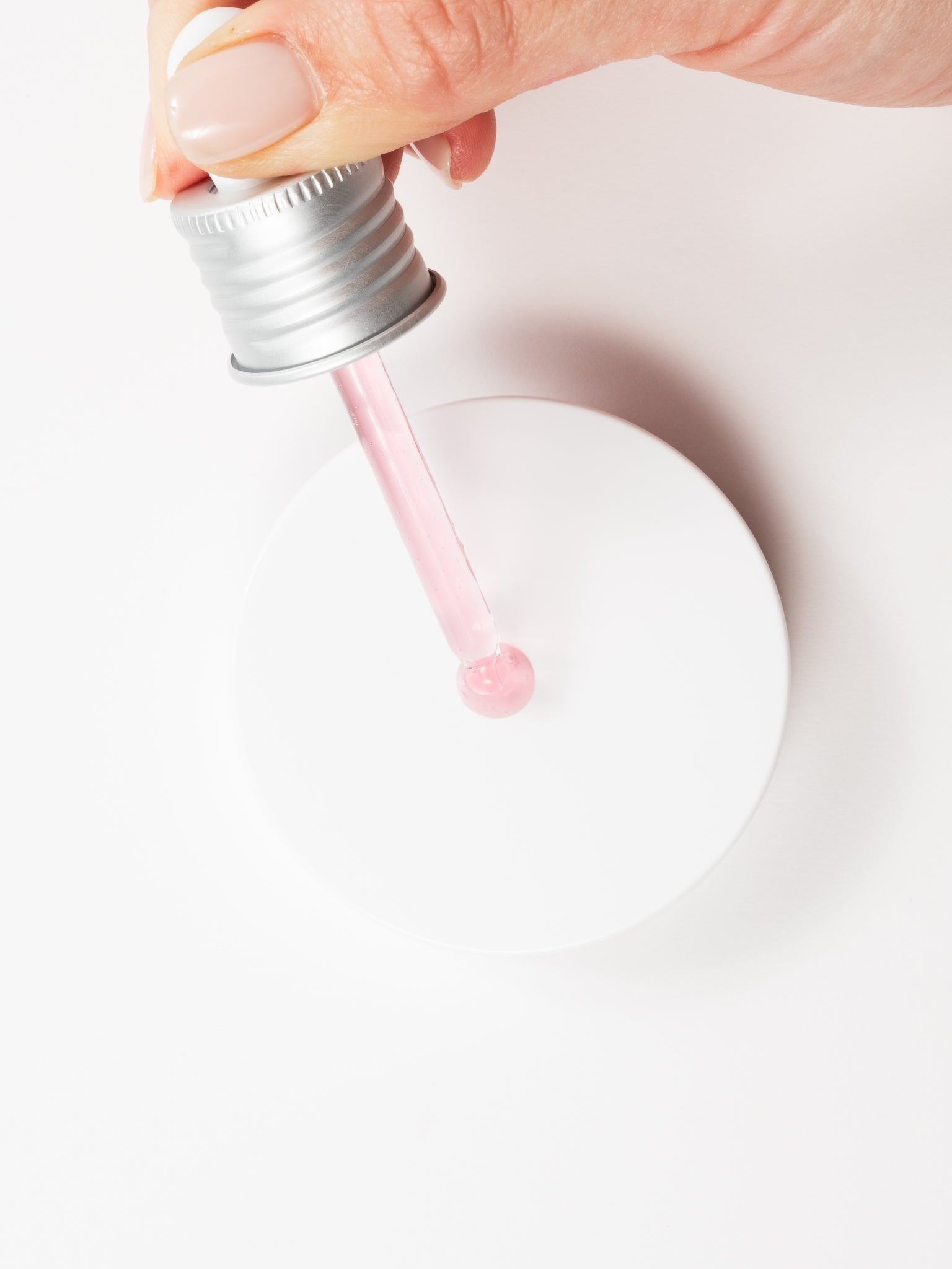 Macro view of a hand applying a drop of Anua Niacinamide 10 + TXA 4 Serum from a silver dropper onto a white surface.