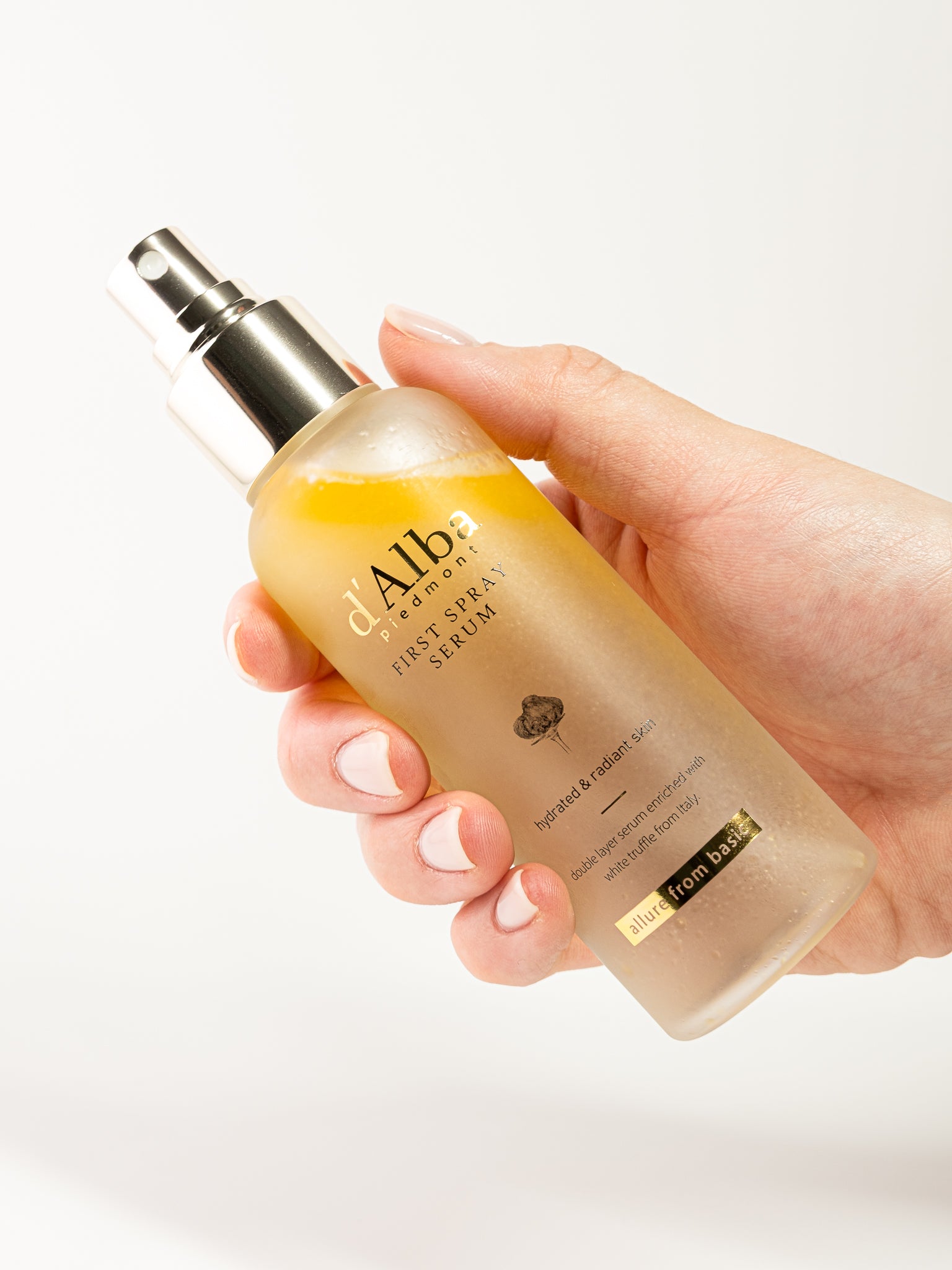 Hand holding the d'alba first spray serum bottle with a blurred background