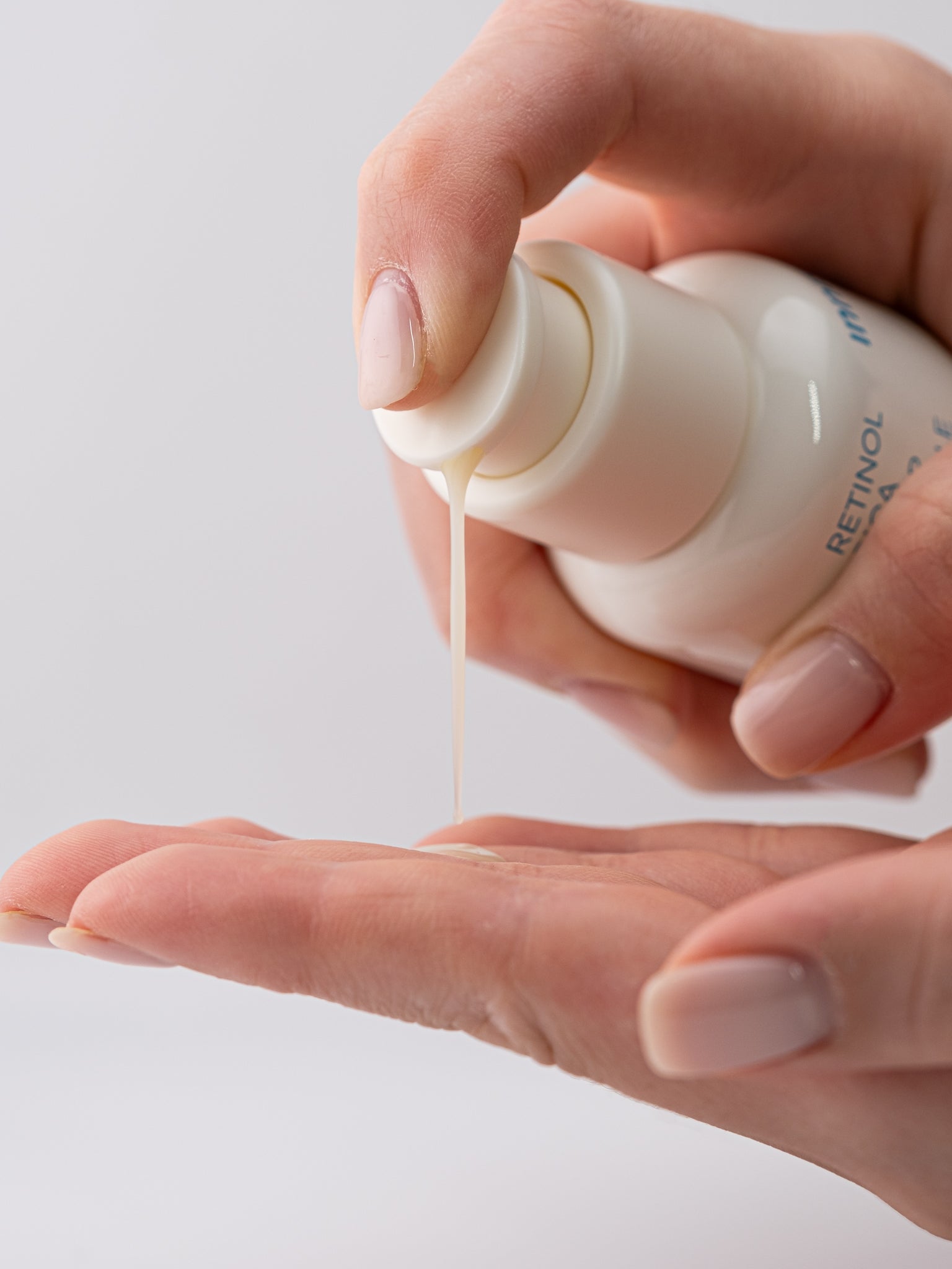 Hand holding a bottle of innisfree retinol cica repair ampoule with dropper over another hand on a light background