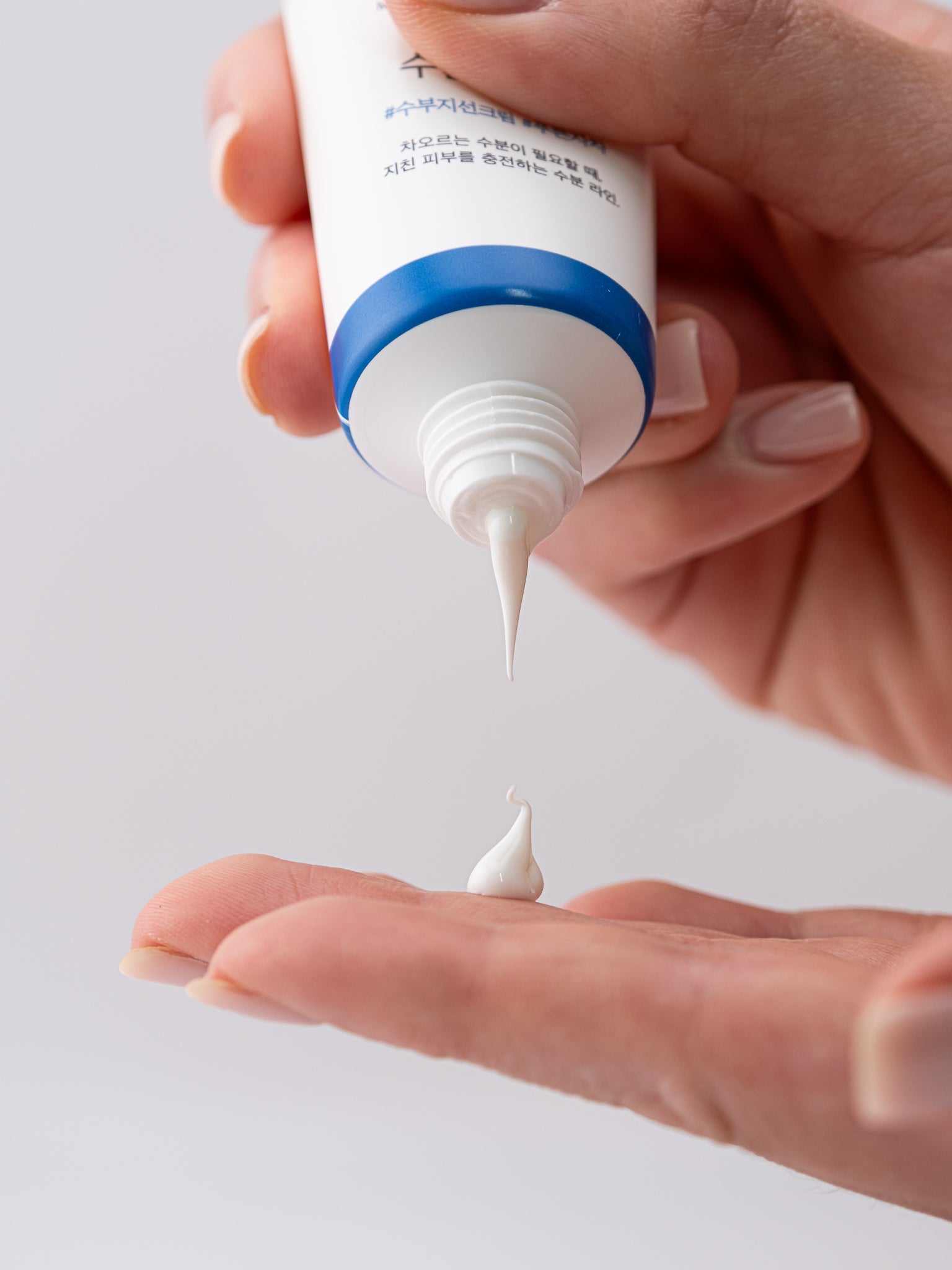 Hand holding a tube of birch juice moisturizing sunscreen with a small amount being squeezed onto the palm against a light background