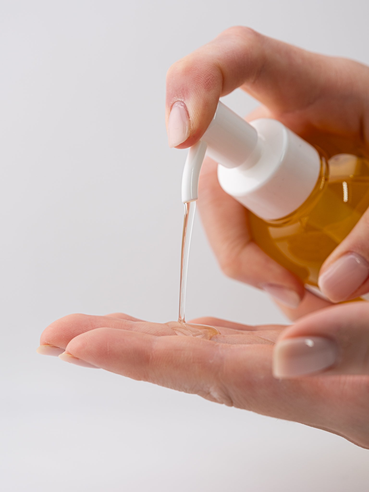 Hand dispensing pure cleansing oil onto another hand on a light background