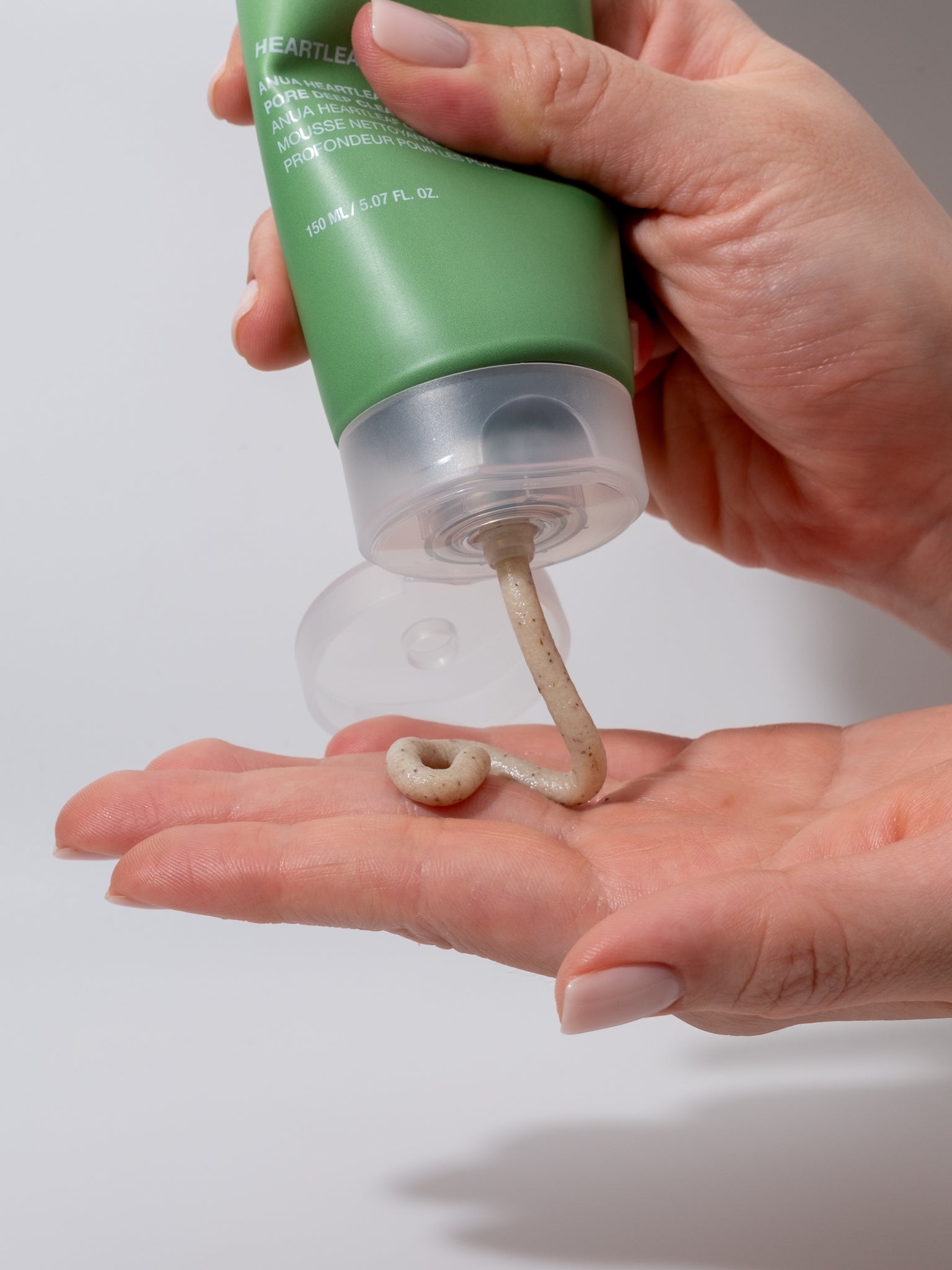 Hand squeezing anua heartleaf pore control cleansing foam onto hand on white background