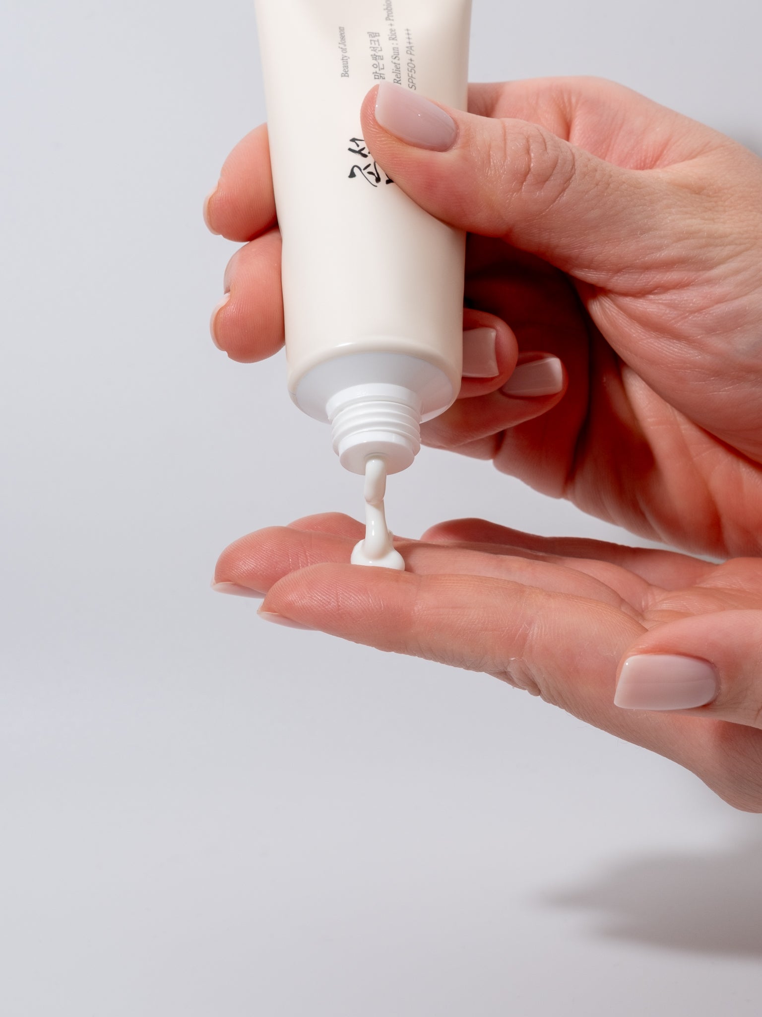 Hand squeezing beauty of joseon relief sun and probiotics with a small amount on the palm against a light gray background