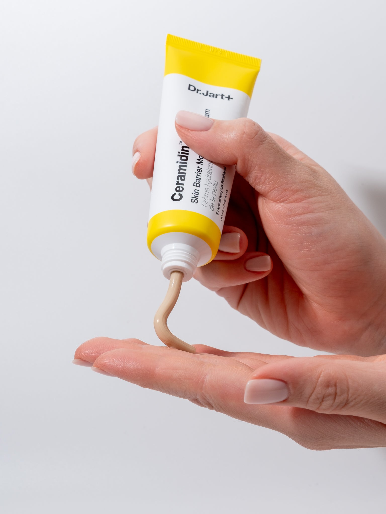 Hand holding a tube of Dr. Jart+ Ceramium Skin Barrier Cream with a white background