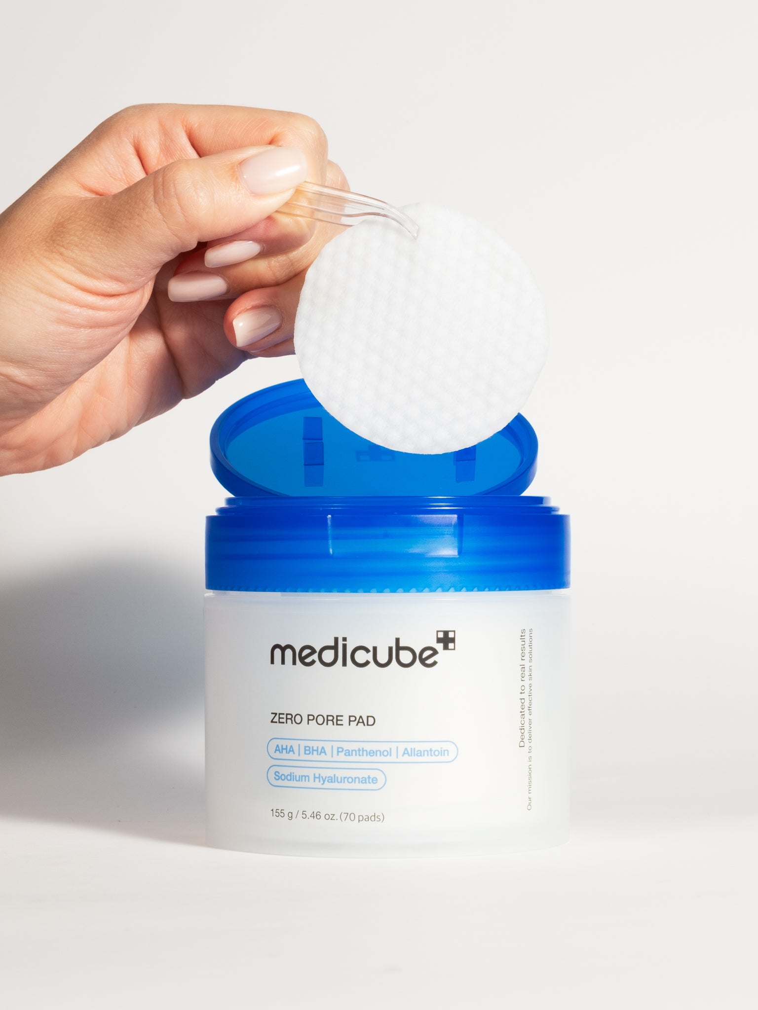 A hand using clear tweezers to lift a Medicube Zero Pore Pad from its open jar.