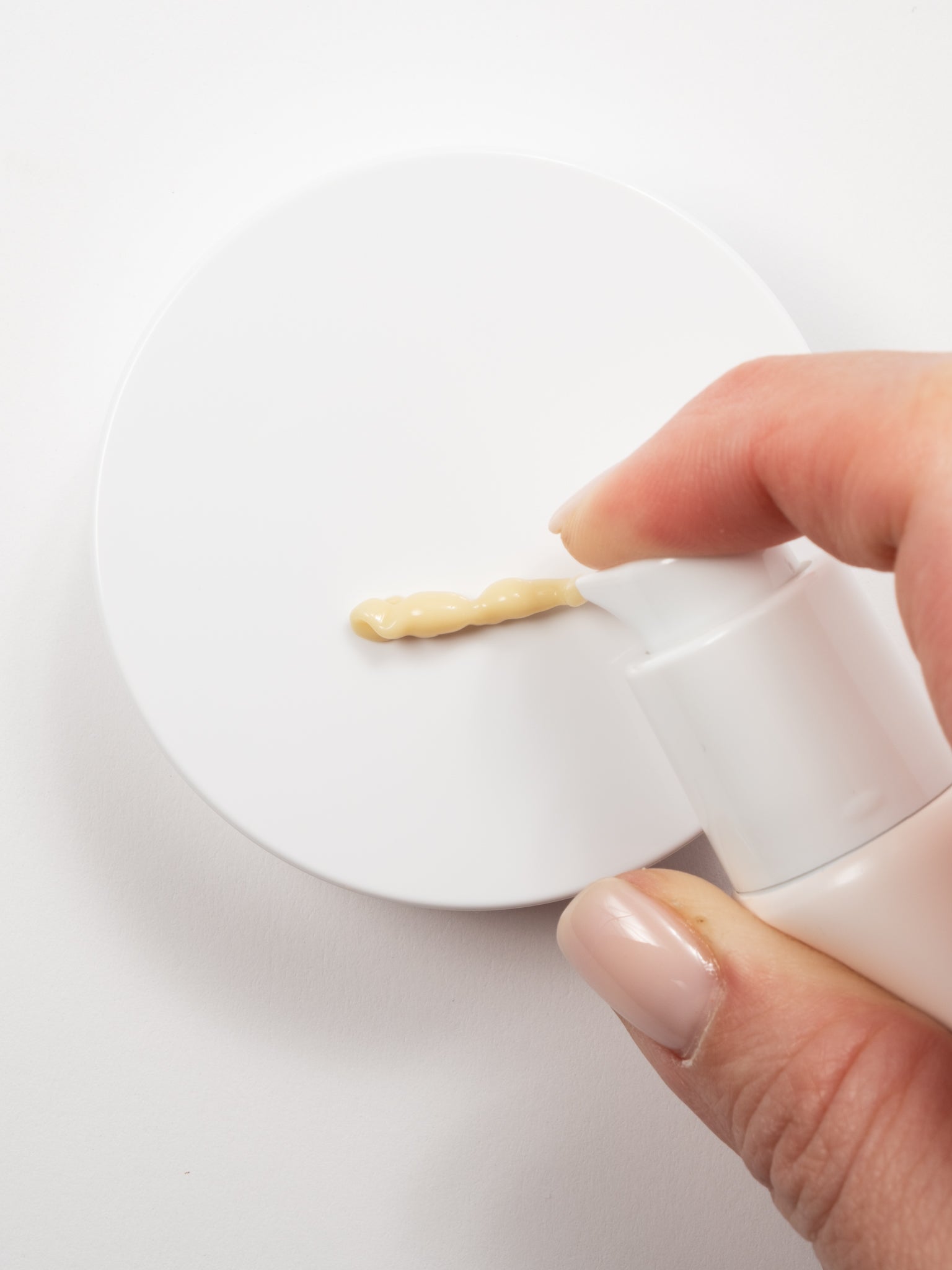 Macro view of a hand dispensing Beauty of Joseon Revive Eye Serum (Ginseng + Retinal) onto a white surface.
